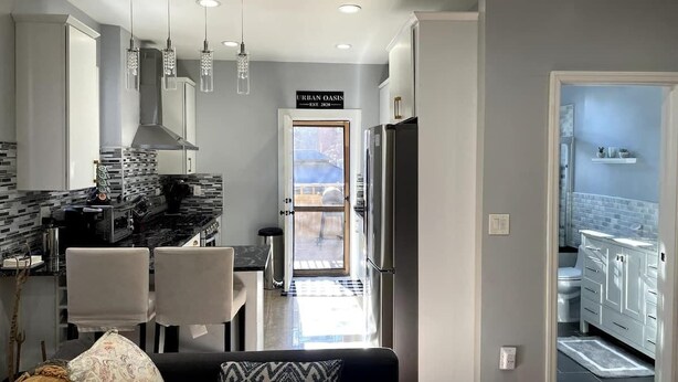 A modern kitchen with a dining area, a living room with a sofa and cushions, and a view of the outdoors. - 3BR NYC-bound Apt, Sleeps 8, Parking (Jersey City)