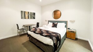 A hotel room with a bed, a desk, a chair, a nightstand, and a wall-mounted mirror. - Ex hotel ensuite room at gouger st 431 (Adelaide)