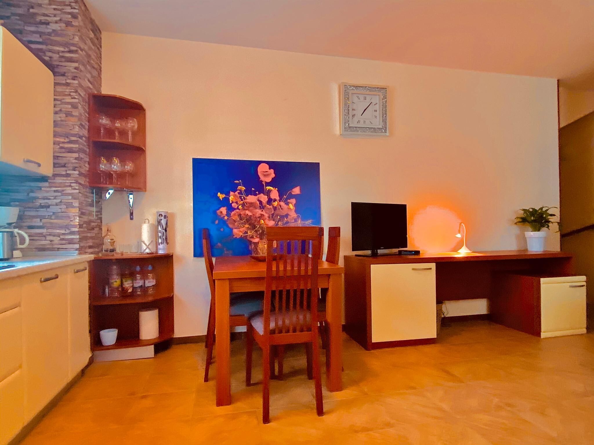 Un salon chaleureux avec une table à manger, des chaises, un téléviseur, une horloge et une petite plante.