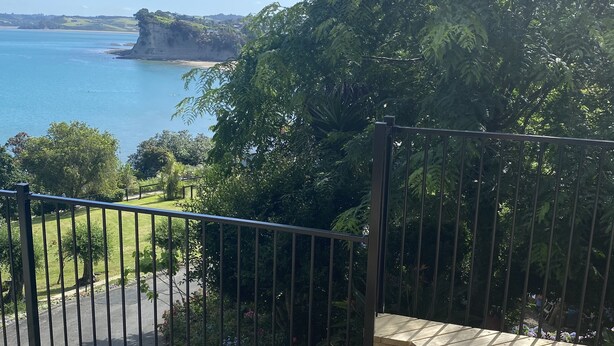 A wooden deck with a metal railing overlooking a body of water and a cliff.