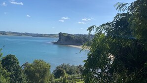 A coastal landscape with a clear sky, a sandy beach, and a rocky outcrop.