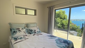 A bedroom with a large bed, a window with curtains, and a view of the sea.