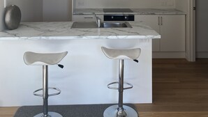 A modern kitchen with white cabinets, a marble countertop, a built-in stove, and pendant lighting.