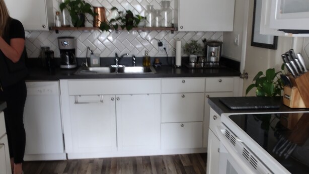 A modern kitchen with white cabinets, a herringbone backsplash, and a wooden floor.