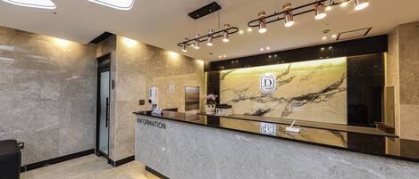 A reception area with a marble counter, a digital information kiosk, and a large mirror reflecting the interior.