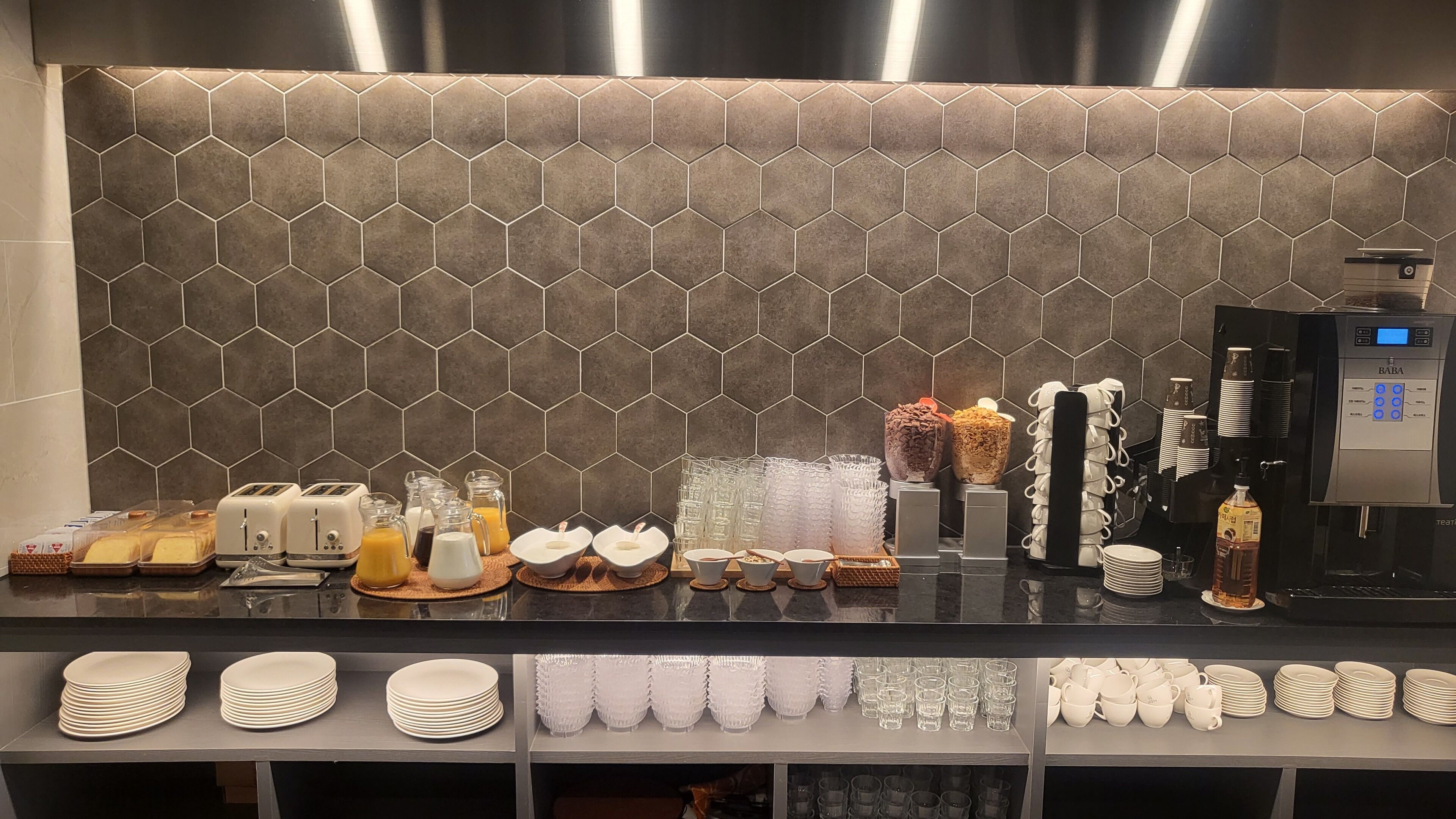A breakfast bar with a hexagonal tile backsplash, a coffee machine, and various breakfast items.
