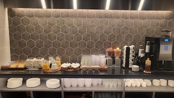 A breakfast bar with a hexagonal tile backsplash, a coffee machine, and various breakfast items.
