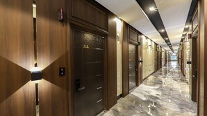 A hotel corridor with wooden doors, numbered room signs, and a marble floor. - Hotel Demer (Mokpo)