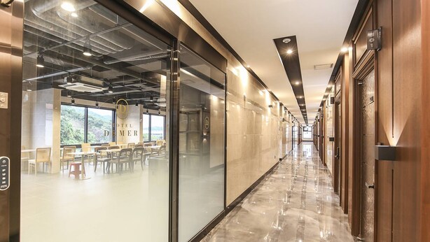 A hotel corridor with glass walls, a dining area, and a view of greenery outside. - Hotel Demer (Mokpo)