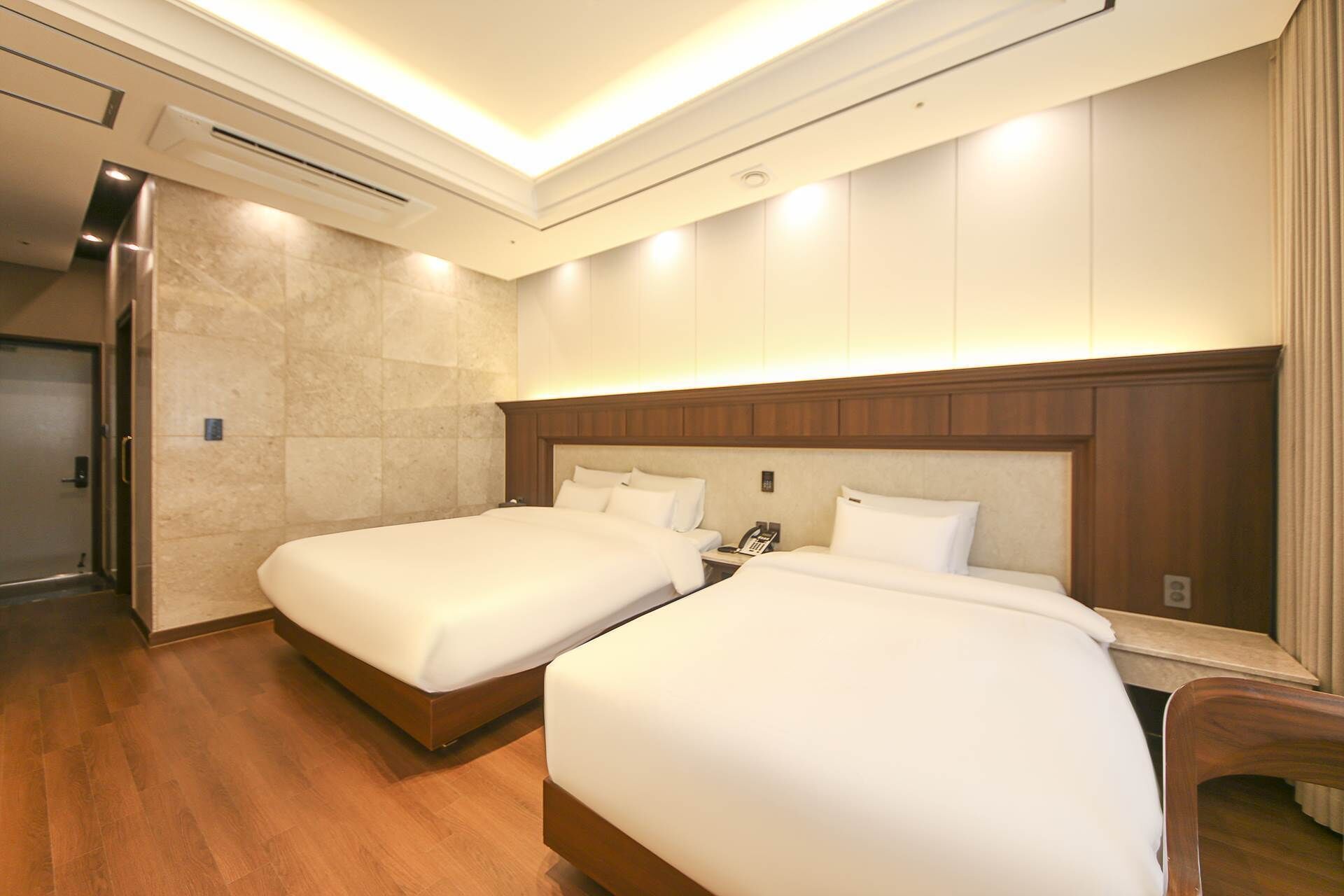 Habitación de hotel con dos camas, cabeceros de madera, piso de madera y un equipo de aire acondicionado instalado en la pared.