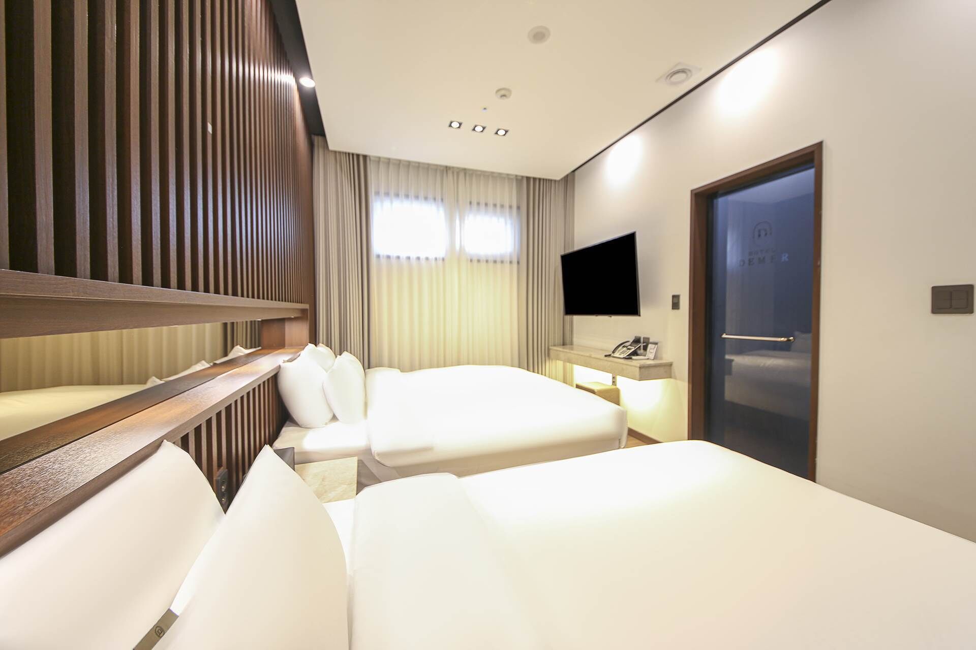 A hotel room with two beds, a TV, a desk with a phone, and a door with a handle.