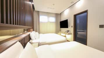 A hotel room with two beds, a TV, a desk with a phone, and a door with a handle.