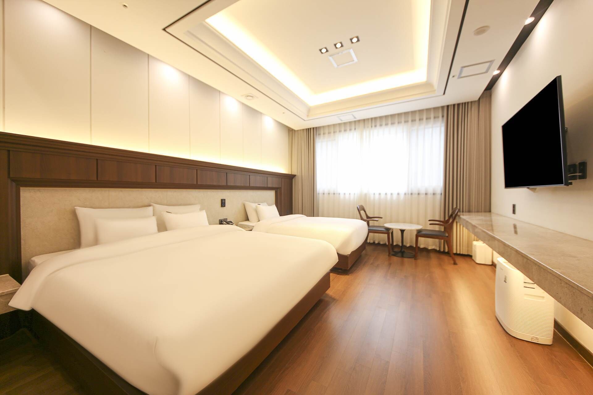 A hotel room with two beds, a TV, a small table, and a chair.
