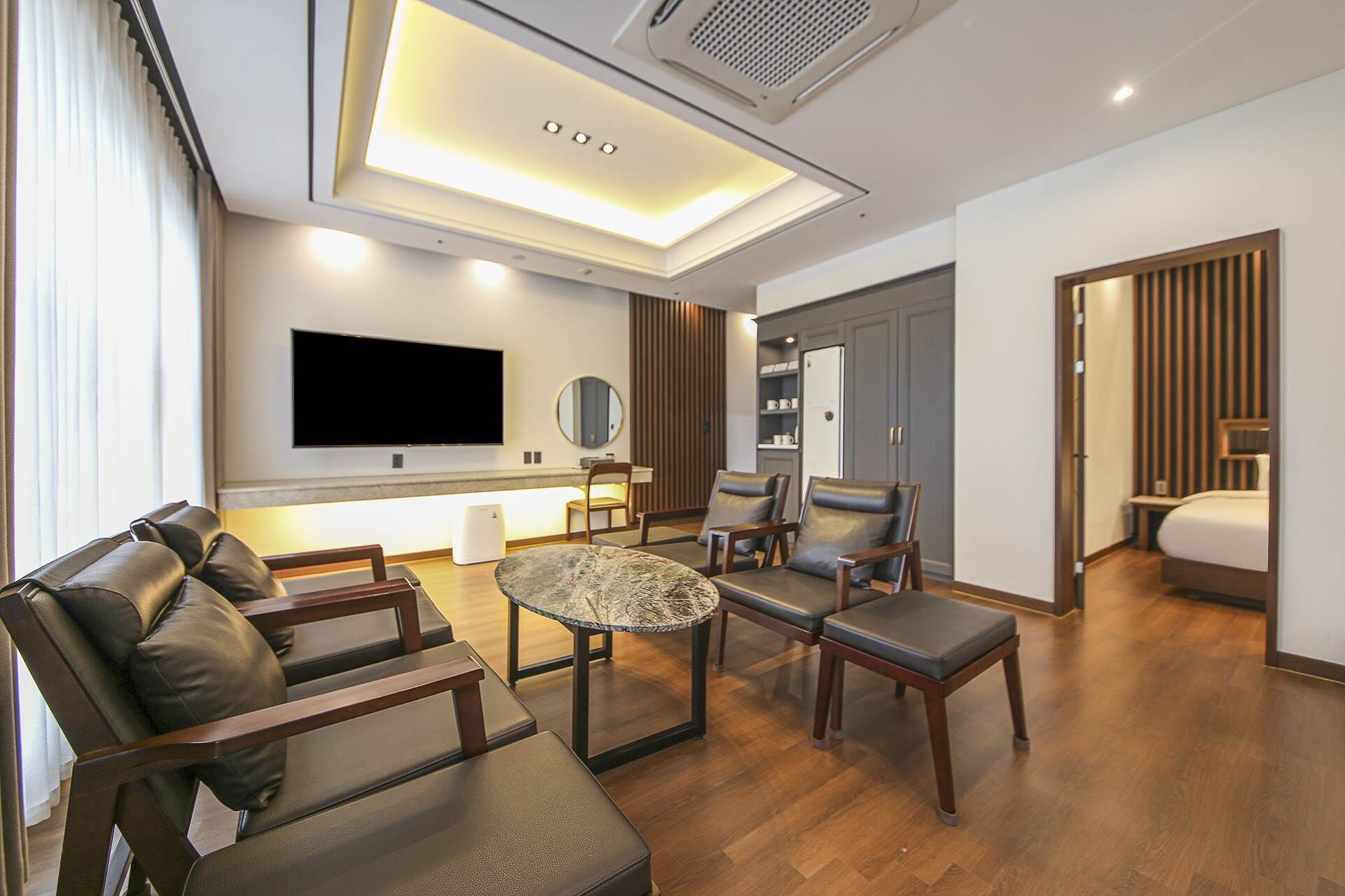 A modern living room with a flat-screen TV, comfortable seating, a coffee table, and a large window with curtains.