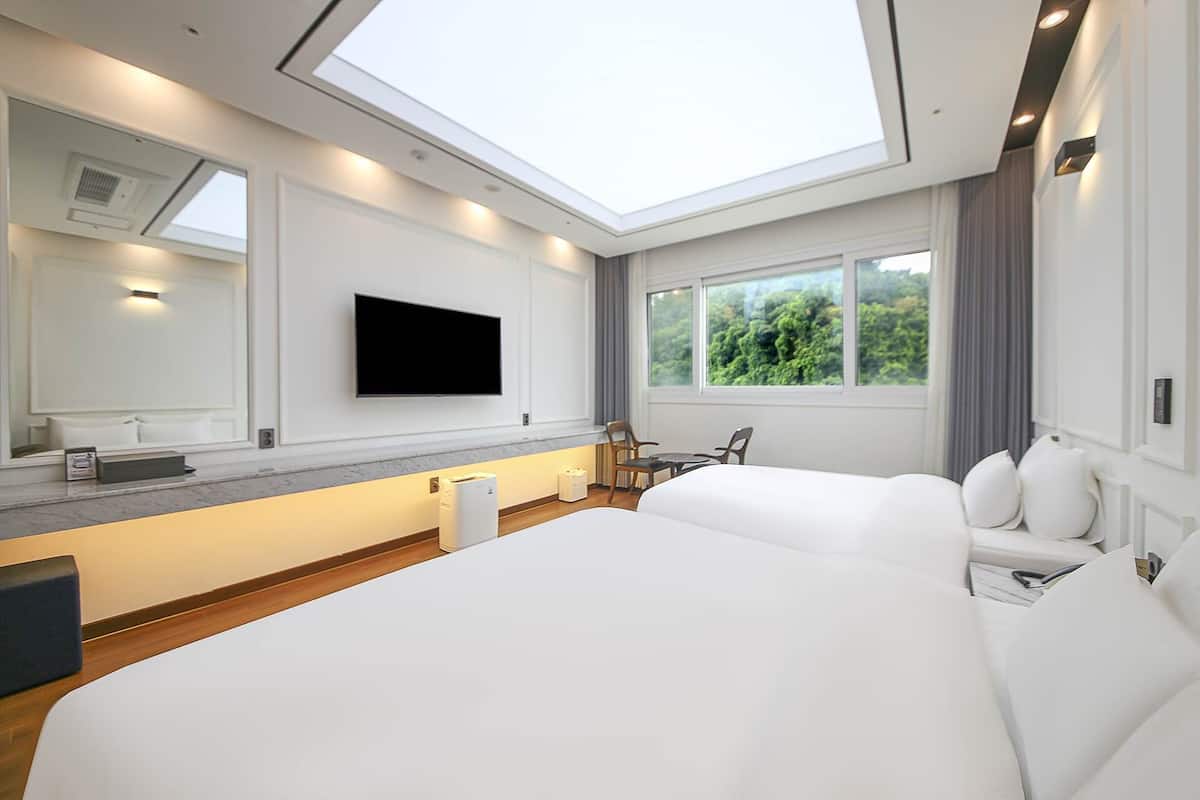 Una habitación de hotel moderna con una cama grande, un televisor de pantalla plana en la pared, un escritorio con una silla y una ventana con vista a zonas verdes.
