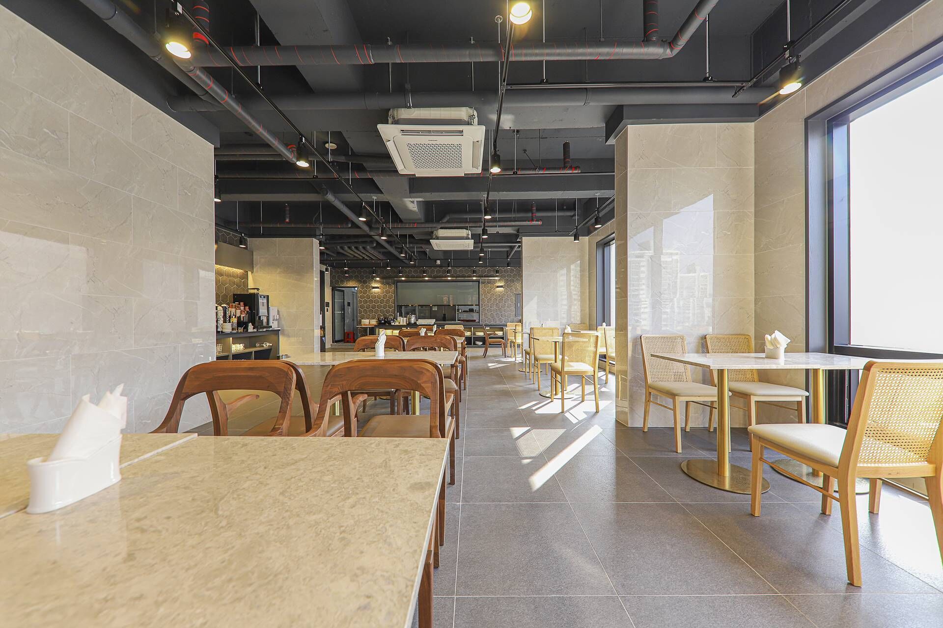 Un interior de restaurante moderno con suelos de baldosas de mármol, sillas de madera y mimbre, y una zona de cocina central.