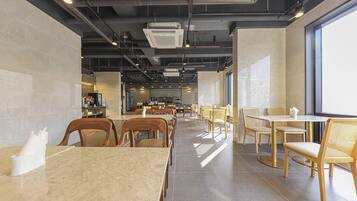Un interior de restaurante moderno con suelos de baldosas de mármol, sillas de madera y mimbre, y una zona de cocina central.
