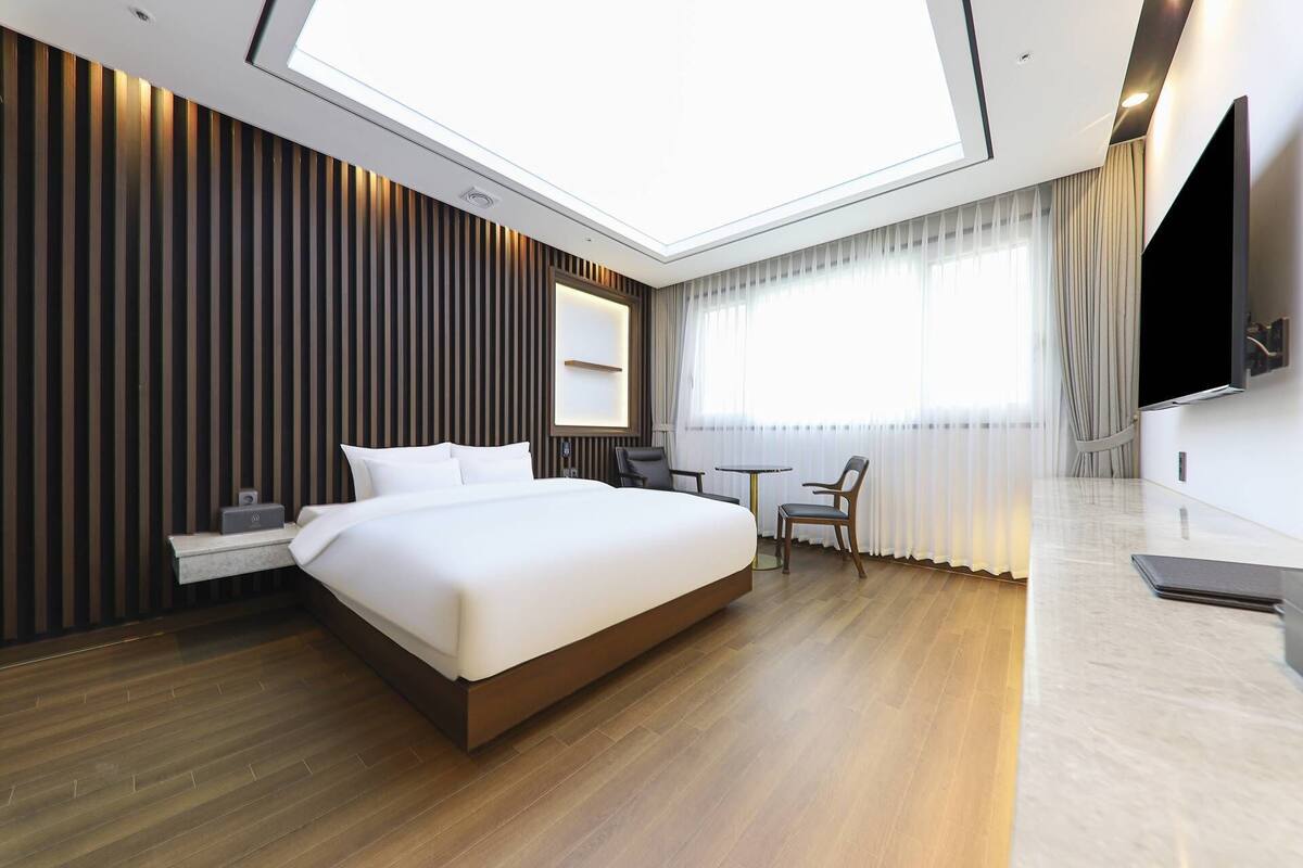 Una habitación de hotel moderna con una cama grande, un escritorio, una silla, un televisor de pantalla plana y un tragaluz.