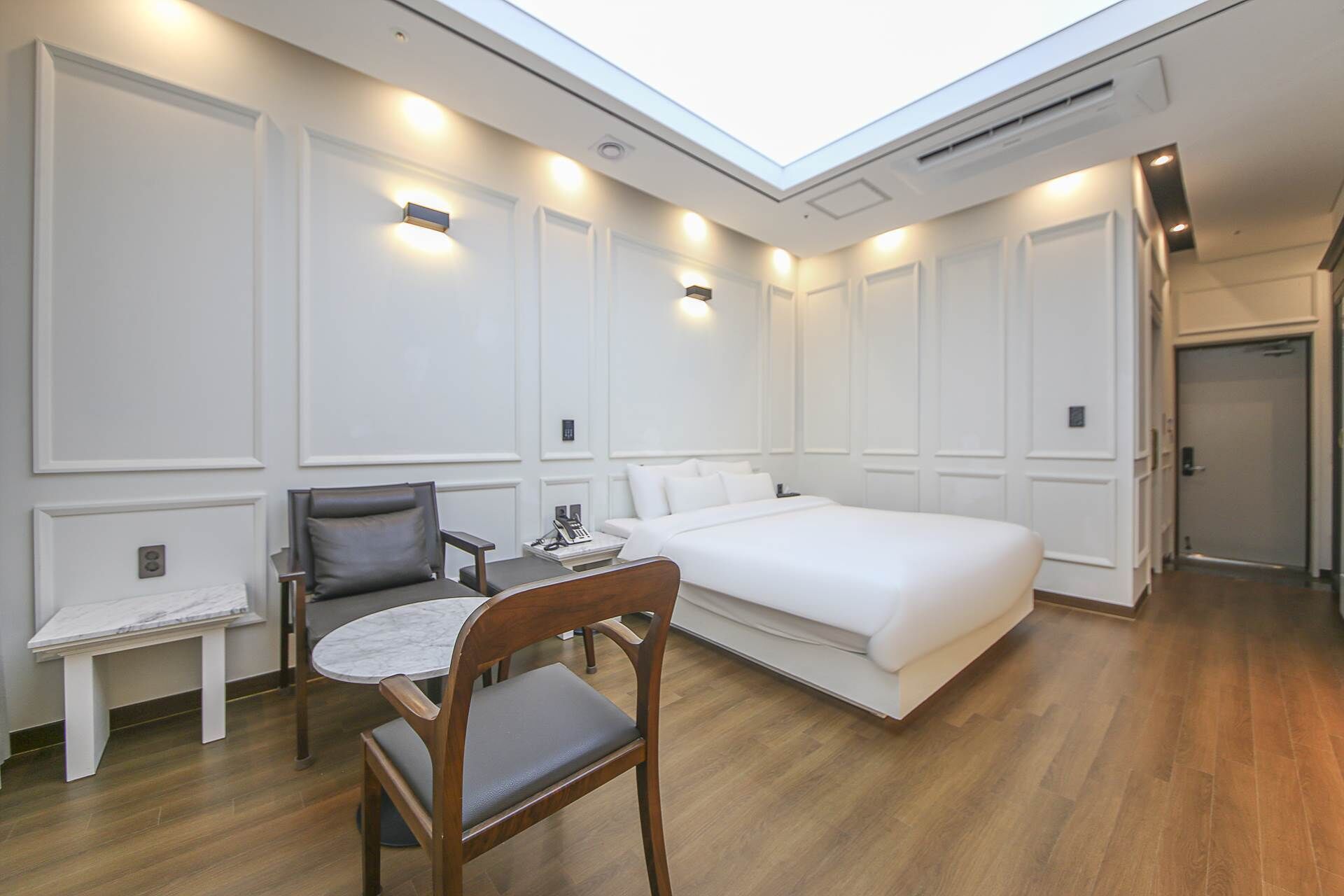 A hotel room with a skylight, a bed, a desk with a chair, and a small table.