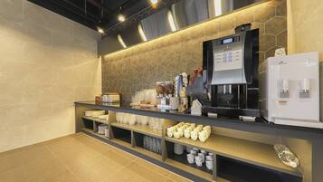 A modern coffee station with a coffee machine, tea dispenser, and various cups and plates.