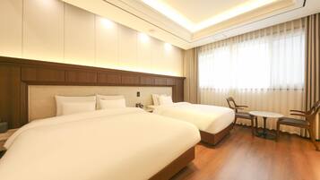A hotel room with two beds, a small table, and a chair.