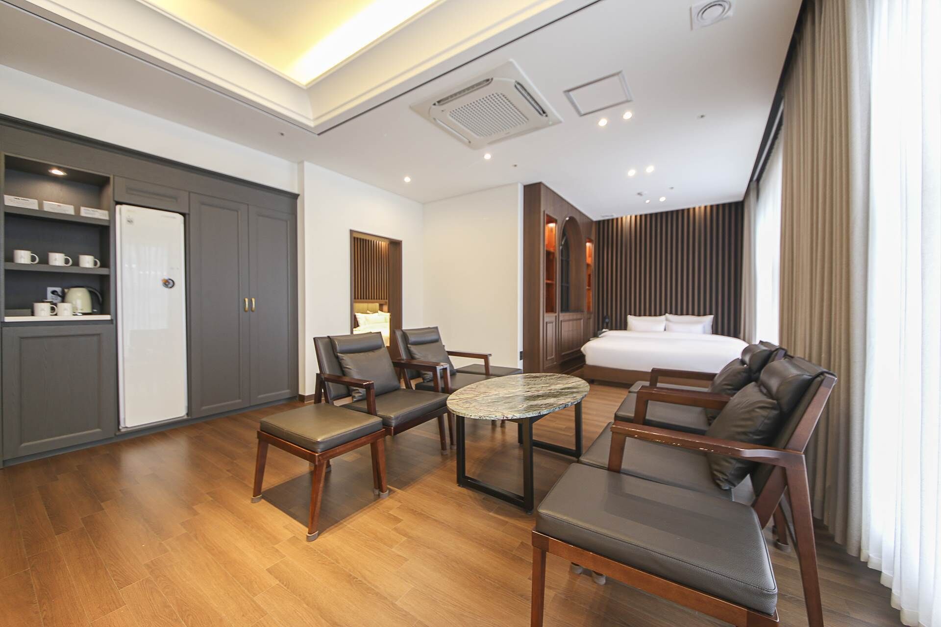 A hotel room with a bed, two armchairs, a small table, a wardrobe, and a shelf with mugs.