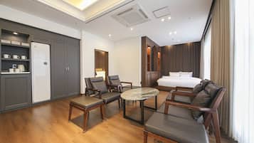 A hotel room with a bed, two armchairs, a small table, a wardrobe, and a shelf with mugs.