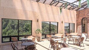 An outdoor patio with wicker furniture, large windows, and hanging plants. - Hotel Demer (Mokpo)