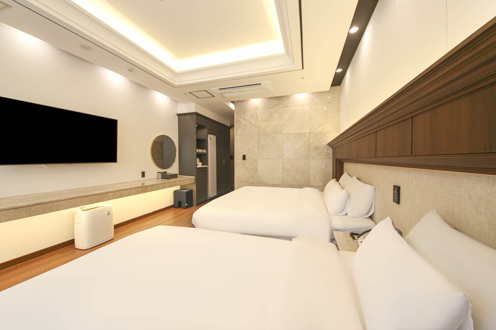 Ein modernes Hotelzimmer mit einem großen Flachbildfernseher an der Wand, einer Minibar, einer kleinen Sitzecke und einem großen Bett mit vielen Kissen.