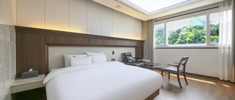 Habitación de hotel con una cama grande, un escritorio y una silla. Se ve vegetación a través de la ventana.