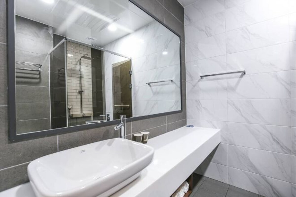 Un baño moderno con un espejo grande, un lavamanos blanco y una zona de ducha.