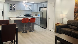 Una cocina moderna con armarios grises, un refrigerador de acero inoxidable y una isla central con dos taburetes rojos.