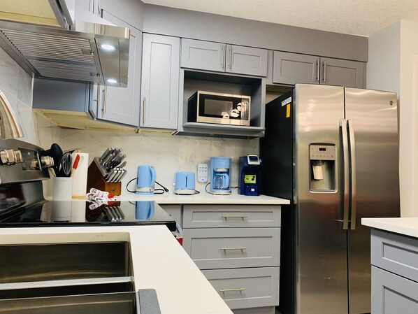 A modern kitchen with grey cabinets, a stainless steel refrigerator, a microwave, and a coffee maker. - Luxurious One Bedroom Suite WindTower (Canmore)