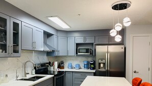 Una cocina moderna con armarios grises, un refrigerador de acero inoxidable, un microondas, una cafetera y un lavamanos.