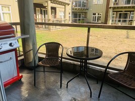 Uma varanda com churrasqueira, duas cadeiras de vime e uma mesa pequena.