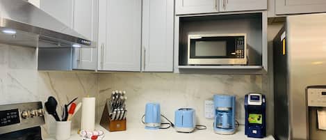 Een moderne keuken met grijze kastjes, een magnetron, een koffiezetapparaat en een fornuis.