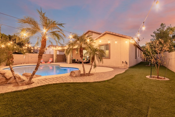A backyard with a swimming pool, palm trees, and string lights.