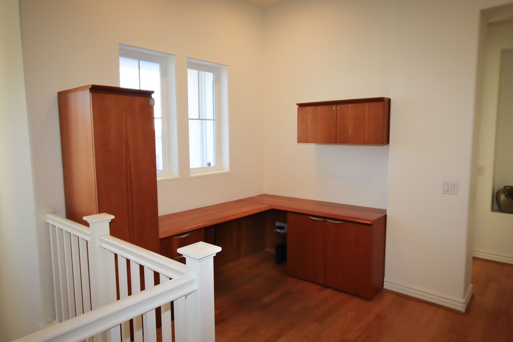 A corner office with a desk, a white railing, and a window.