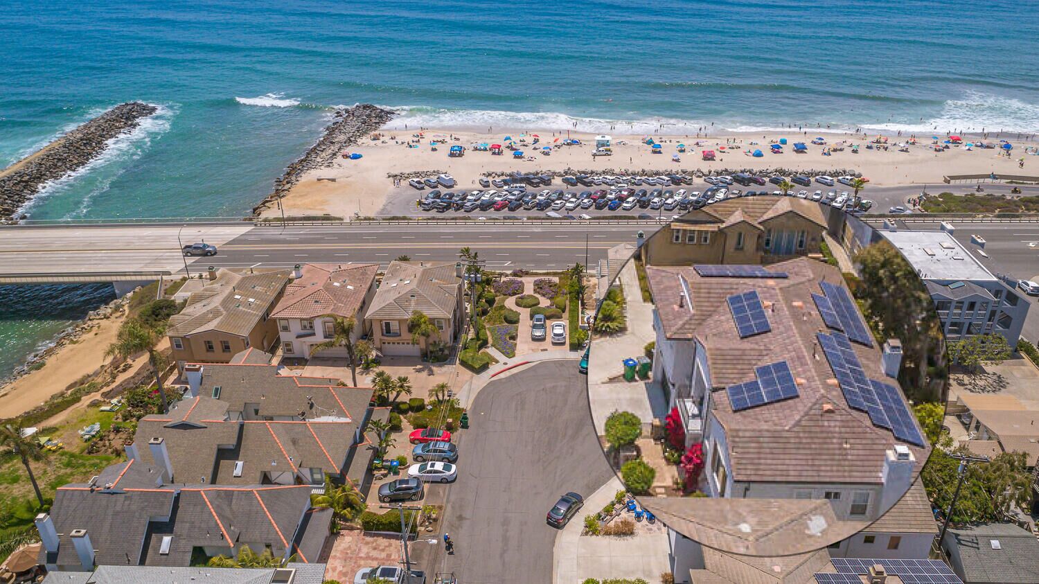 Zona residencial costera con casas, una playa y coches aparcados.