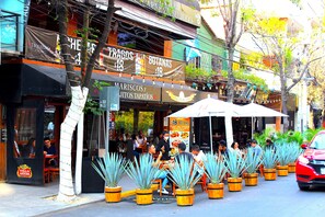 Une rue avec des terrasses, des plantes en pot et différentes boutiques.