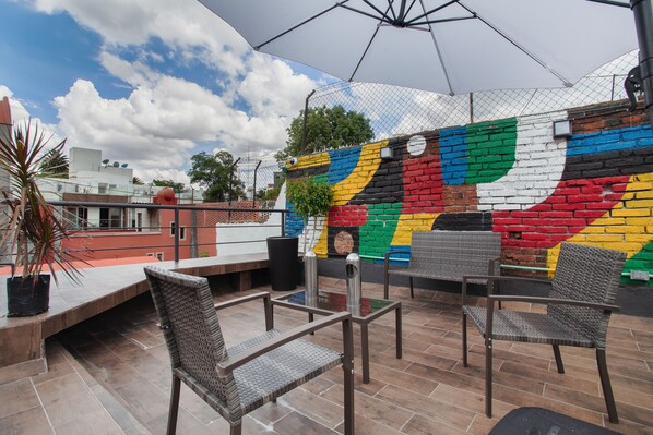 Un espace extérieur aménagé en terrasse, avec des chaises en osier, une table et une fresque colorée sur le mur.