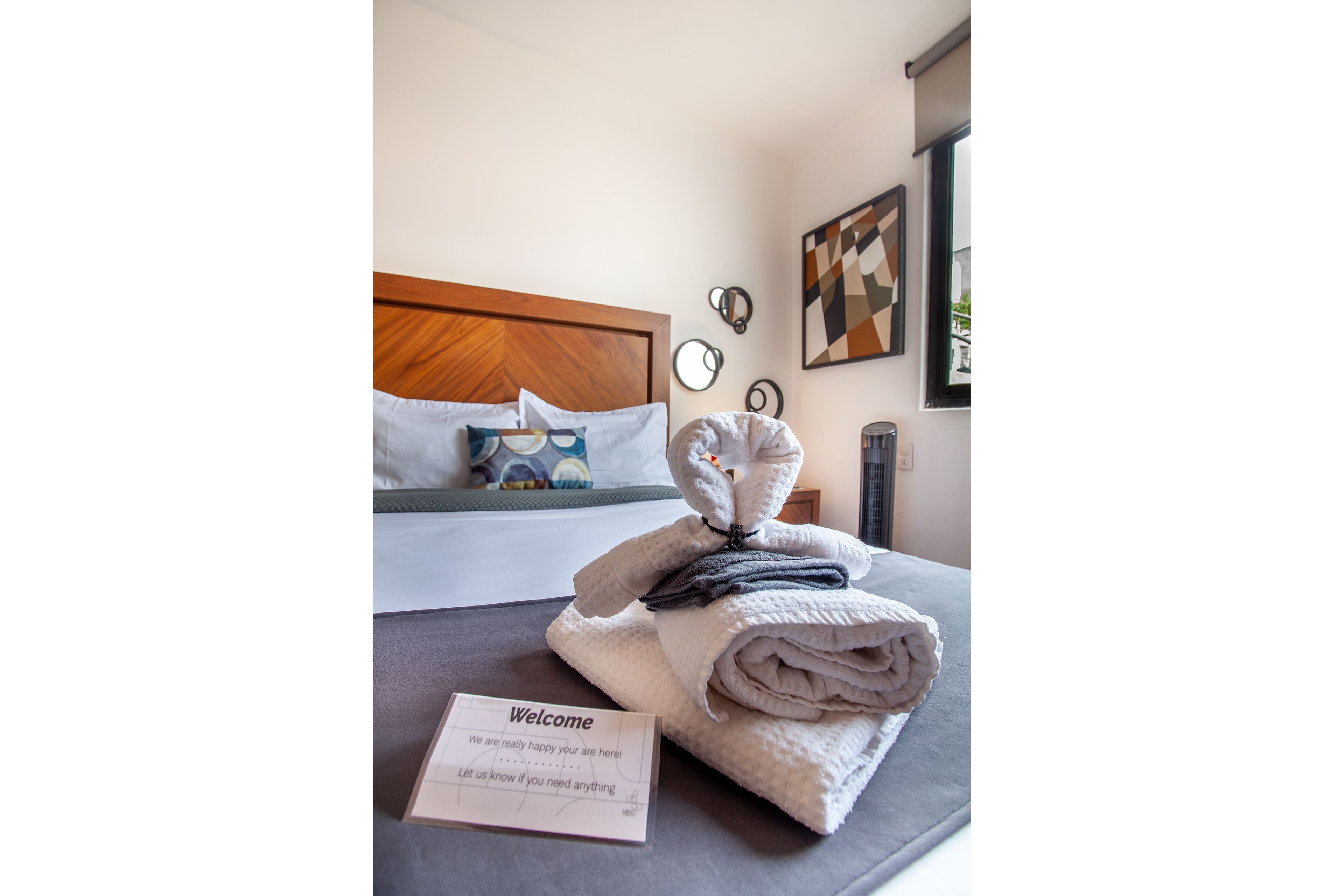 A neatly made bed with a folded towel and a welcome card on a gray bedspread.