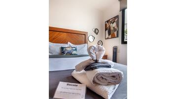 A neatly made bed with a folded towel and a welcome card on a gray bedspread.