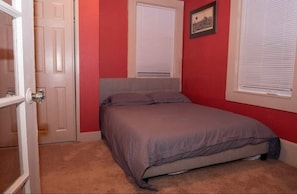 A bedroom with a bed, a door, and a window with blinds.