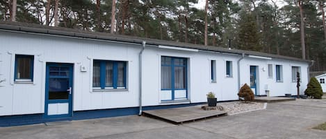 A row of white mobile homes with blue trim, numbered doors, and a small front porch area.
