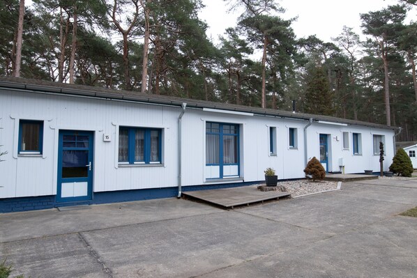Une rangée de maisons mobiles blanches, avec des bordures bleues, des portes numérotées et un petit porche à l’avant.
