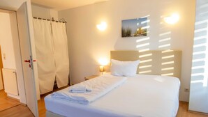 Una cama bien hecha con sábanas blancas, una lámpara de noche y un cuadro colgado en la pared.