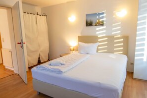 Een net opgemaakt bed met witte lakens, een bedlampje en een aan de muur hangend schilderij.