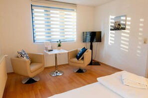 Een hotelkamer met een bed, twee fauteuils, een tafeltje, een televisie en een raam met zonwering.