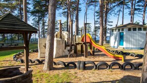 Un parque infantil con tobogán, zona de juegos con neumáticos y un pequeño refugio.